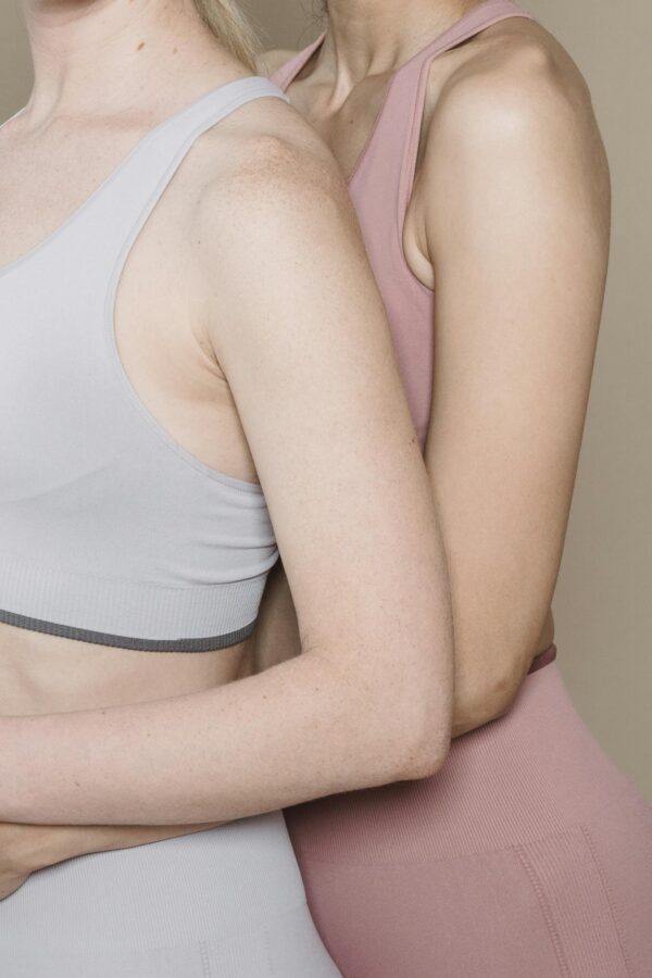 Studio shot of two women modeling modern activewear against a beige backdrop.