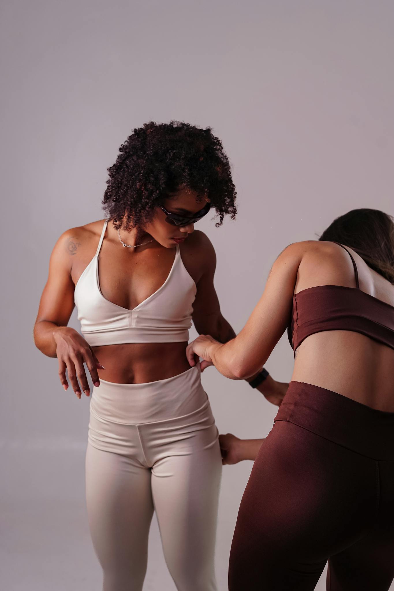 Two women adjusting fitness clothing during a fitting session indoors.